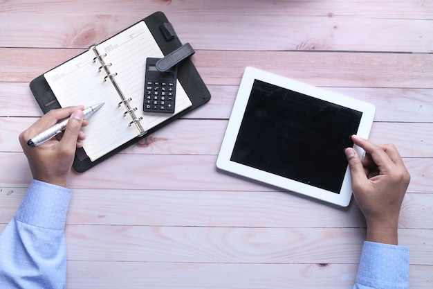 A person making notes on a notebook, representing manual budgeting versus a variety of financial apps shown on a tablet, highlighting the convenience and features offered by them.