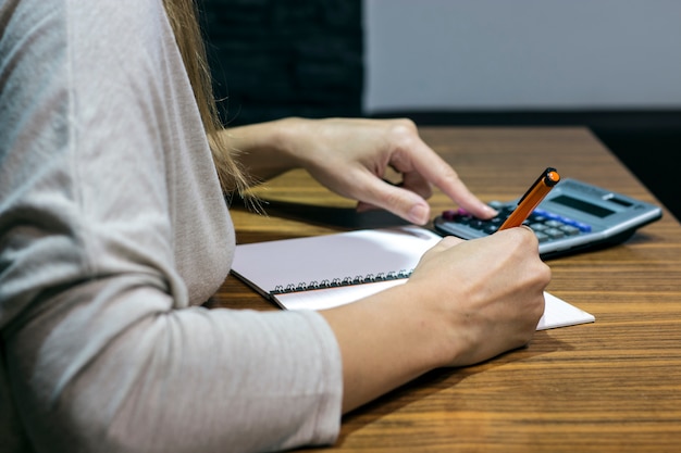 A person reviewing bank statements at a table, highlighting specific transactions. A calculator and pen are also visible on the table