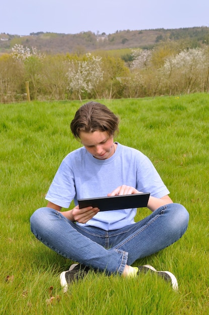A young student in a rural setting is using a tablet to access online educational resources. The environment is simple, but the student's focused expression demonstrates the transformative potential of EdTech in underserved communities.