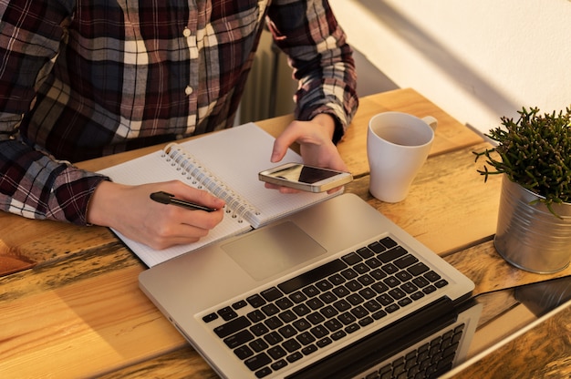 A person sitting at a table, using a laptop to plan their shopping list and digital coupons, with a notepad nearby.