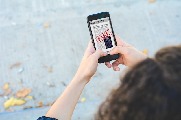 A close-up of a person's hands nervously scrolling through news headlines on a smartphone, with a blurred background.