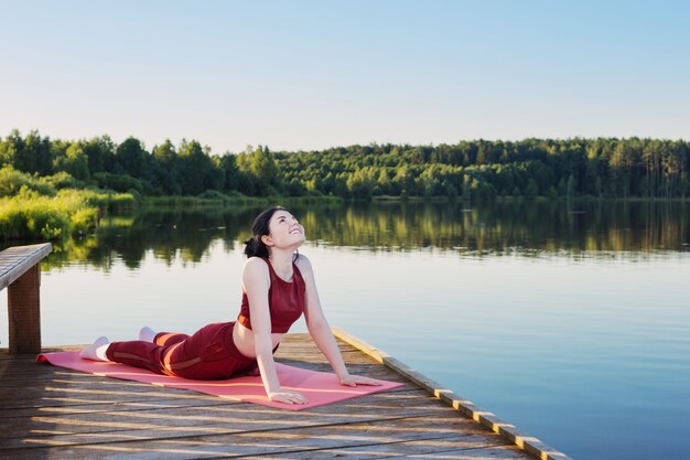 A person practicing yoga outside in a peaceful setting, with a clear blue sky and trees in the background.