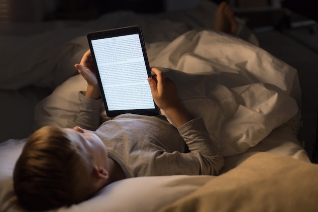 A person using a Calm app on a tablet in bed, listening to a sleep story. The room is dimly lit, and the app interface displays a calming image of a starry night.
