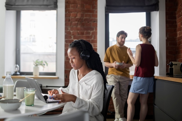 A diverse group of individuals working at a co-working space, all wearing different types of noise-canceling headphones, illustrating focused work and concentration amidst a collaborative environment.