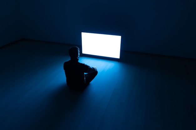 A silhouette of a person sitting alone in front of a computer screen in a darkened room, conveying a sense of isolation and addiction.